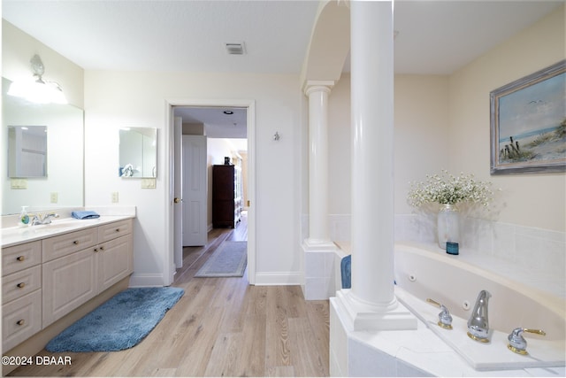 bathroom with ornate columns, hardwood / wood-style floors, vanity, and tiled bath