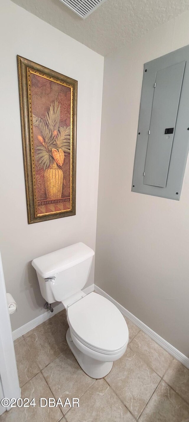 bathroom featuring electric panel, tile patterned floors, a textured ceiling, and toilet