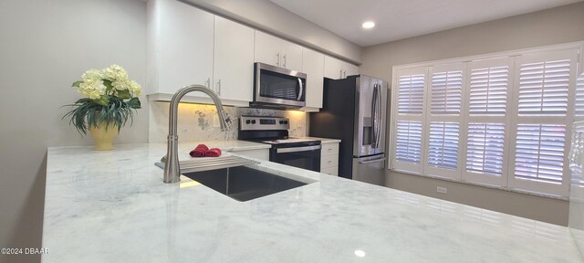 kitchen featuring light stone counters, stainless steel appliances, backsplash, sink, and white cabinets