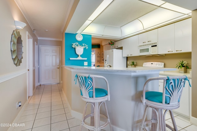 kitchen with light tile patterned flooring, white cabinetry, ornamental molding, a kitchen bar, and white appliances