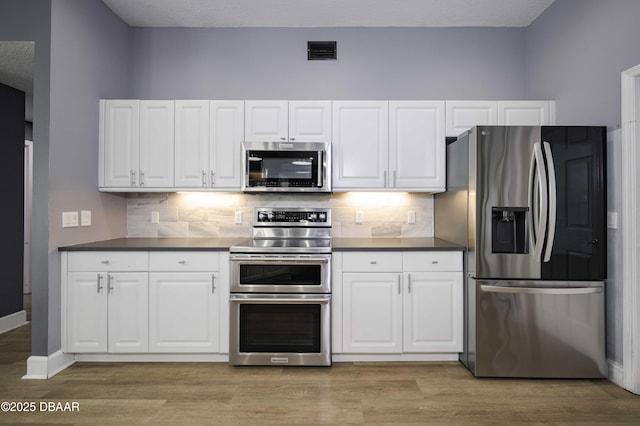 kitchen featuring visible vents, appliances with stainless steel finishes, white cabinets, and dark countertops