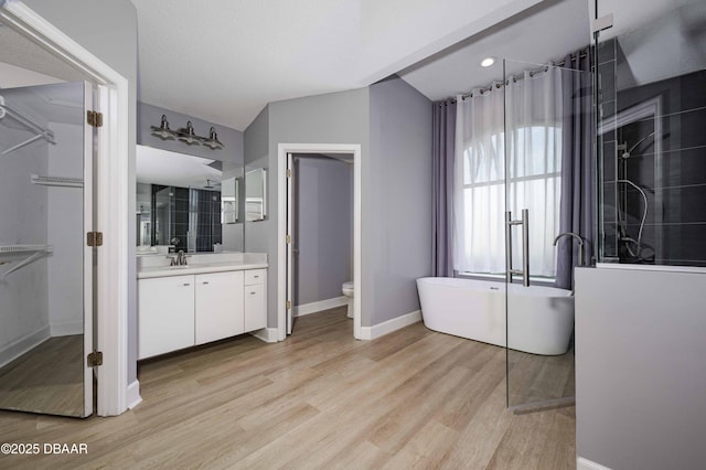bathroom with vanity, lofted ceiling, wood finished floors, baseboards, and a soaking tub