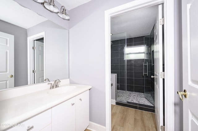 full bathroom featuring vanity, baseboards, tiled shower, and wood finished floors