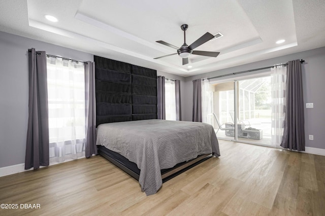 bedroom featuring a tray ceiling, access to exterior, baseboards, and multiple windows