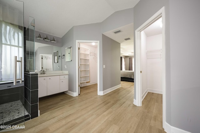 bathroom with visible vents, vanity, baseboards, wood finished floors, and vaulted ceiling