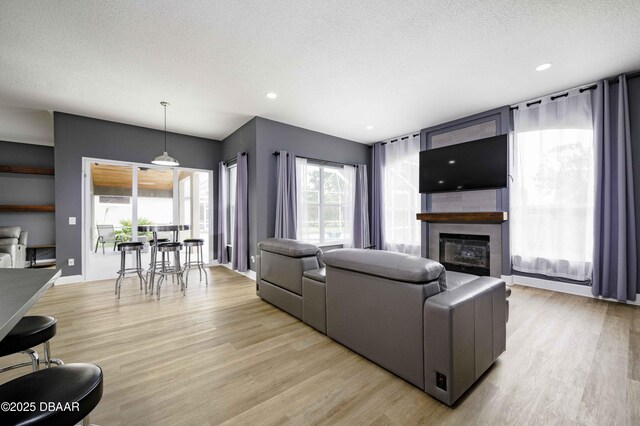 living area with recessed lighting, a textured ceiling, a large fireplace, and light wood finished floors