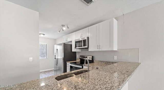 kitchen with light stone counters, stainless steel appliances, visible vents, white cabinets, and tasteful backsplash