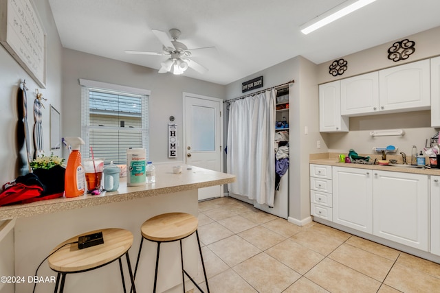 kitchen featuring a kitchen breakfast bar, light tile patterned flooring, ceiling fan, and white cabinetry