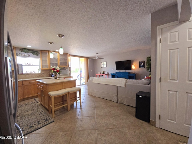 interior space featuring ceiling fan, light countertops, freestanding refrigerator, open floor plan, and glass insert cabinets