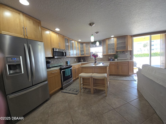 kitchen featuring glass insert cabinets, a center island, light countertops, tasteful backsplash, and appliances with stainless steel finishes