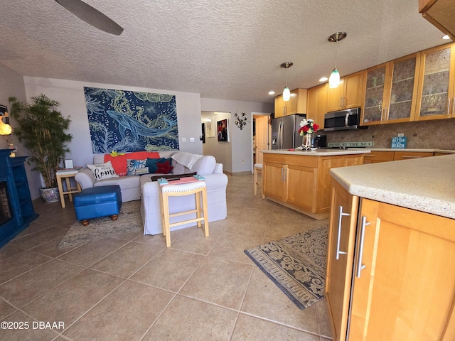 kitchen with a kitchen island, a textured ceiling, appliances with stainless steel finishes, light tile patterned floors, and light countertops