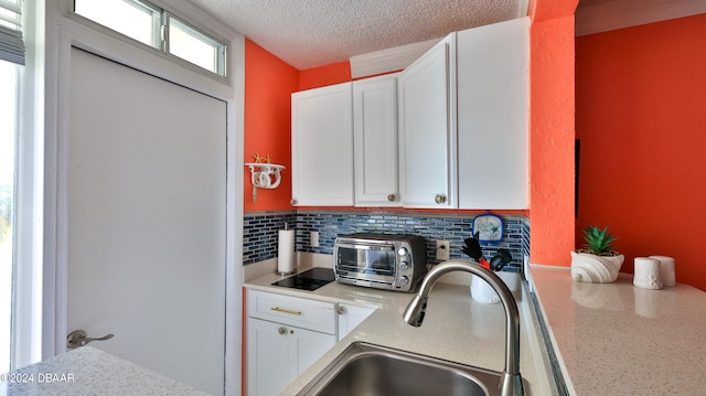 kitchen with light stone counters, backsplash, a textured ceiling, sink, and white cabinets