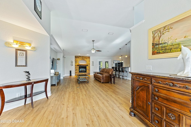 living room with ceiling fan, light wood-type flooring, a fireplace, and vaulted ceiling