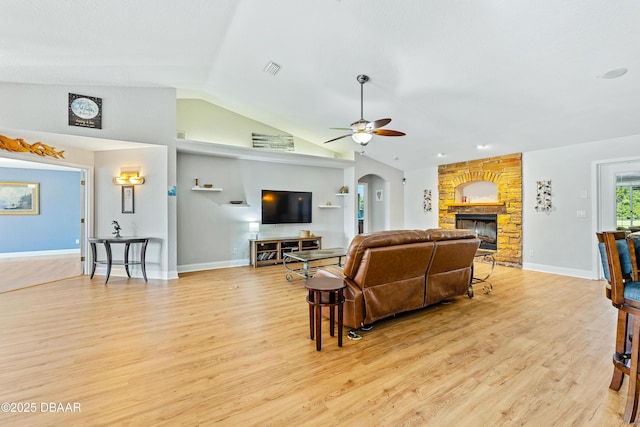 living room featuring ceiling fan, light hardwood / wood-style floors, a stone fireplace, and vaulted ceiling