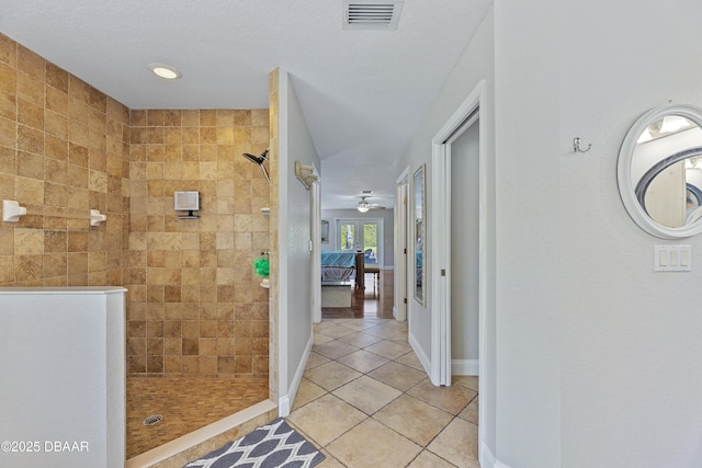 bathroom featuring tile patterned flooring, ceiling fan, a tile shower, and a textured ceiling