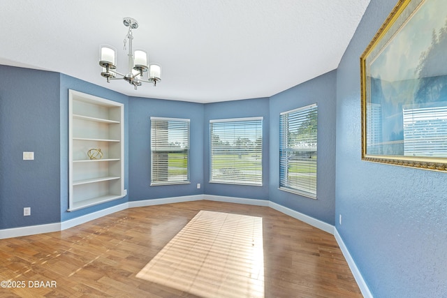 unfurnished dining area with hardwood / wood-style floors, a textured ceiling, built in features, and a notable chandelier