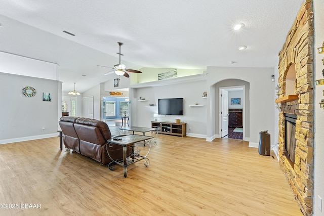 living room with a textured ceiling, ceiling fan with notable chandelier, light hardwood / wood-style flooring, a fireplace, and lofted ceiling