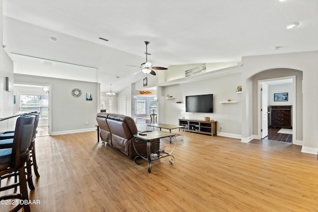 living room with a textured ceiling, ceiling fan with notable chandelier, light hardwood / wood-style floors, and vaulted ceiling