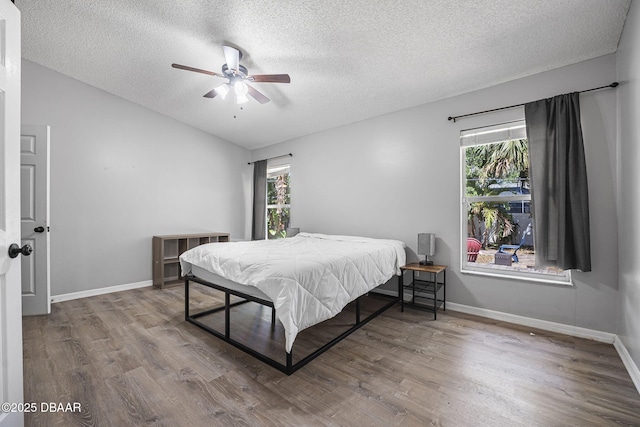 bedroom featuring a textured ceiling, wood finished floors, baseboards, and multiple windows