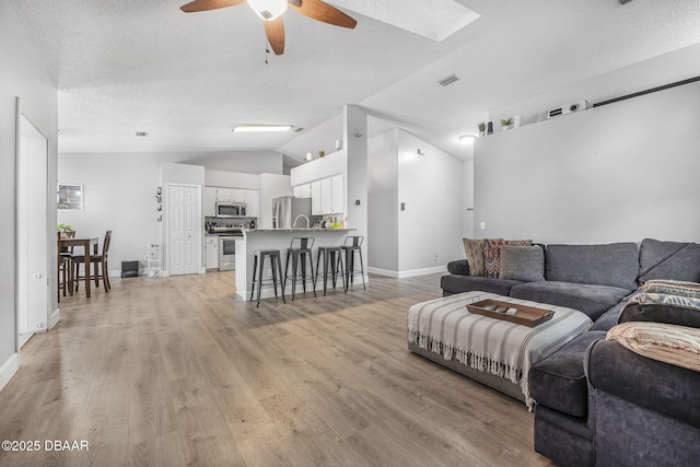 living area featuring lofted ceiling, visible vents, light wood finished floors, a ceiling fan, and baseboards