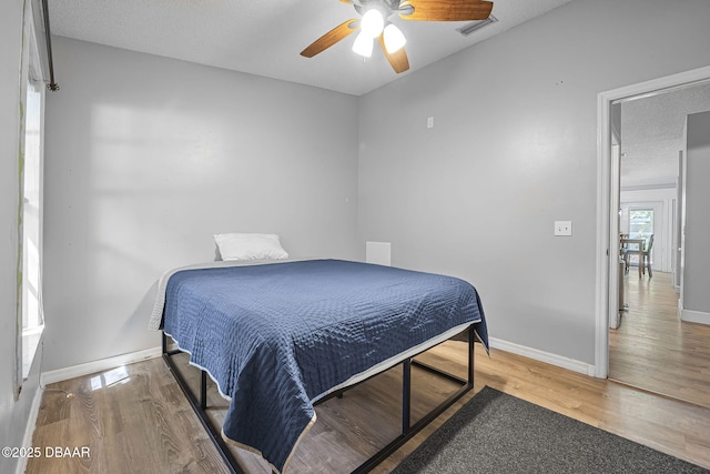 bedroom featuring ceiling fan, baseboards, visible vents, and wood finished floors
