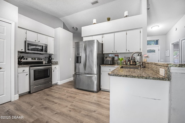 kitchen with a sink, lofted ceiling, stainless steel appliances, white cabinets, and light wood-style floors