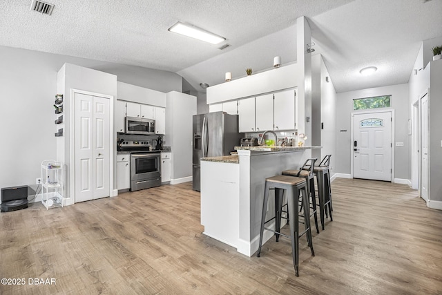 kitchen with a peninsula, stainless steel appliances, a breakfast bar, visible vents, and white cabinetry