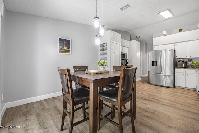 dining space with light wood finished floors, a textured ceiling, visible vents, baseboards, and lofted ceiling