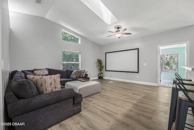 cinema room with a textured ceiling, baseboards, ceiling fan, wood finished floors, and vaulted ceiling with skylight