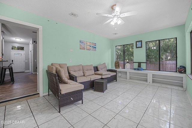 living room with a ceiling fan, baseboards, visible vents, and a textured ceiling