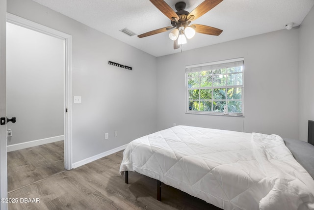 bedroom with baseboards, a ceiling fan, visible vents, and wood finished floors
