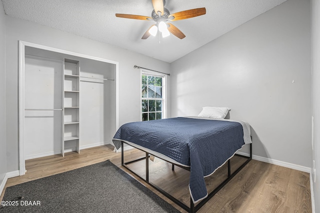 bedroom with a ceiling fan, a textured ceiling, baseboards, vaulted ceiling, and wood finished floors