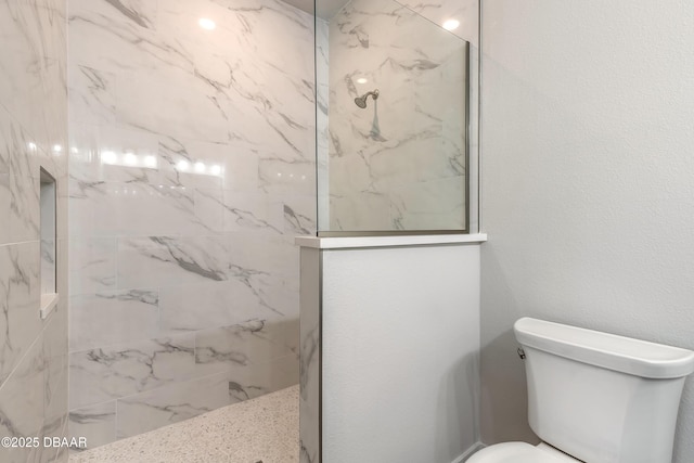 bathroom with a tile shower and toilet