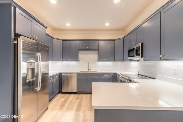 kitchen with sink, decorative backsplash, appliances with stainless steel finishes, light hardwood / wood-style floors, and kitchen peninsula