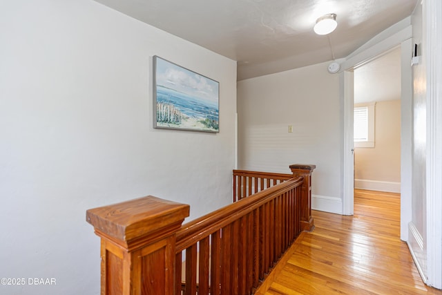 corridor with light wood-type flooring, baseboards, and an upstairs landing