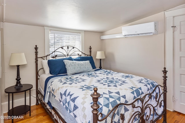 bedroom with a wall unit AC, vaulted ceiling, baseboards, and wood finished floors