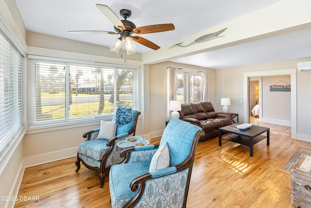 living room featuring ceiling fan, light wood-type flooring, a wall unit AC, and baseboards