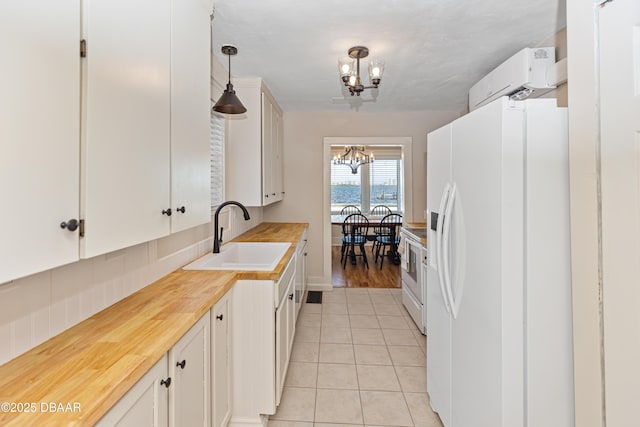 kitchen featuring light tile patterned floors, a notable chandelier, white appliances, a sink, and an AC wall unit