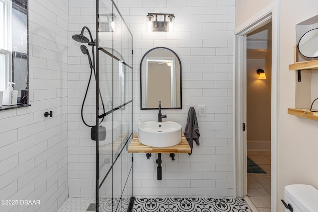 bathroom with tile walls, toilet, tile patterned flooring, a walk in shower, and a sink