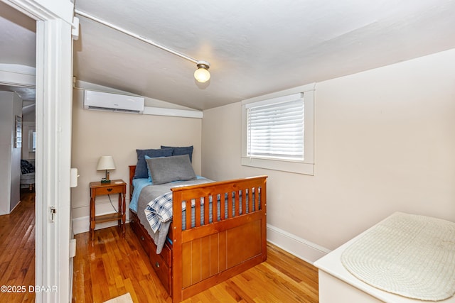 bedroom with lofted ceiling, a wall mounted air conditioner, wood finished floors, and baseboards