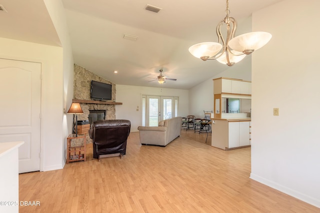 living room featuring ceiling fan with notable chandelier, a fireplace, vaulted ceiling, and light wood-type flooring