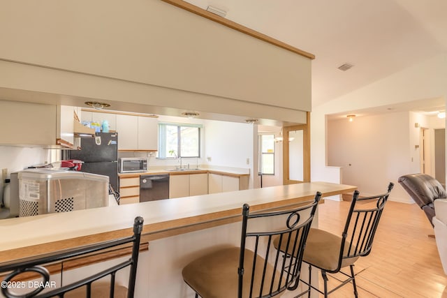 kitchen with vaulted ceiling, white cabinetry, sink, black appliances, and light hardwood / wood-style flooring