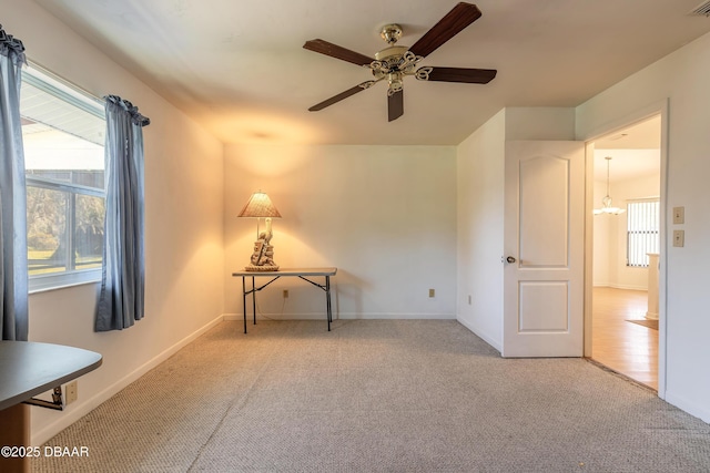 spare room featuring ceiling fan with notable chandelier and light colored carpet