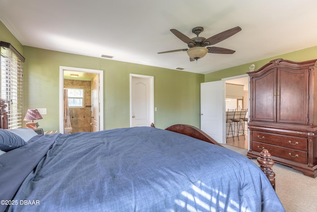 bedroom with ensuite bathroom, light colored carpet, and ceiling fan