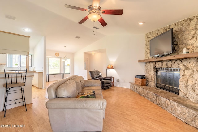 living room with vaulted ceiling, a stone fireplace, ceiling fan, and light wood-type flooring