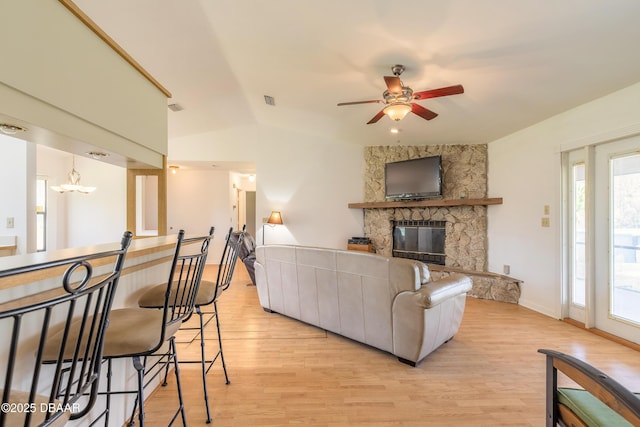 living room featuring lofted ceiling, a stone fireplace, ceiling fan with notable chandelier, and light wood-type flooring