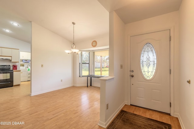 entrance foyer with washer / clothes dryer, lofted ceiling, a notable chandelier, and light hardwood / wood-style floors