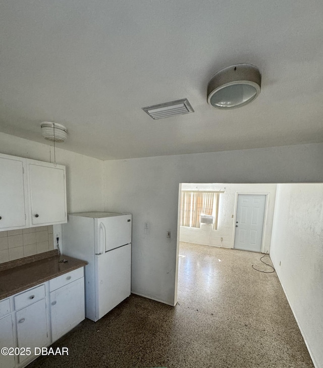 kitchen with dark countertops, visible vents, cooling unit, freestanding refrigerator, and white cabinetry