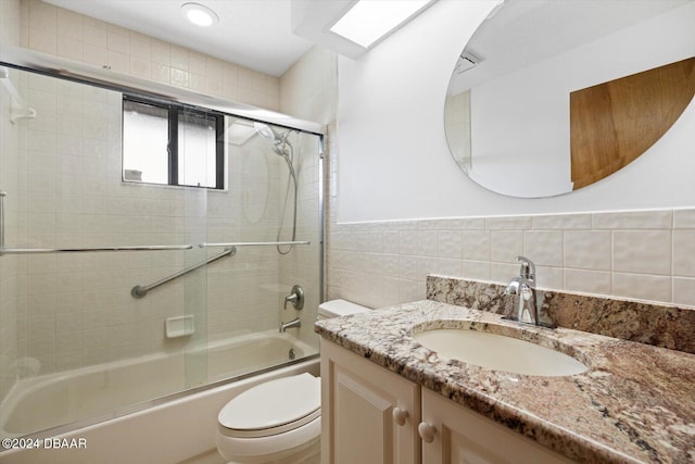 full bathroom with vanity, combined bath / shower with glass door, tile walls, and toilet