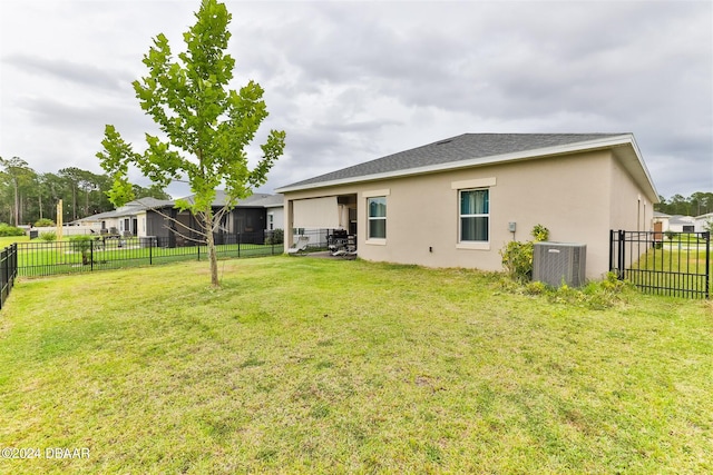 rear view of property with central air condition unit and a yard